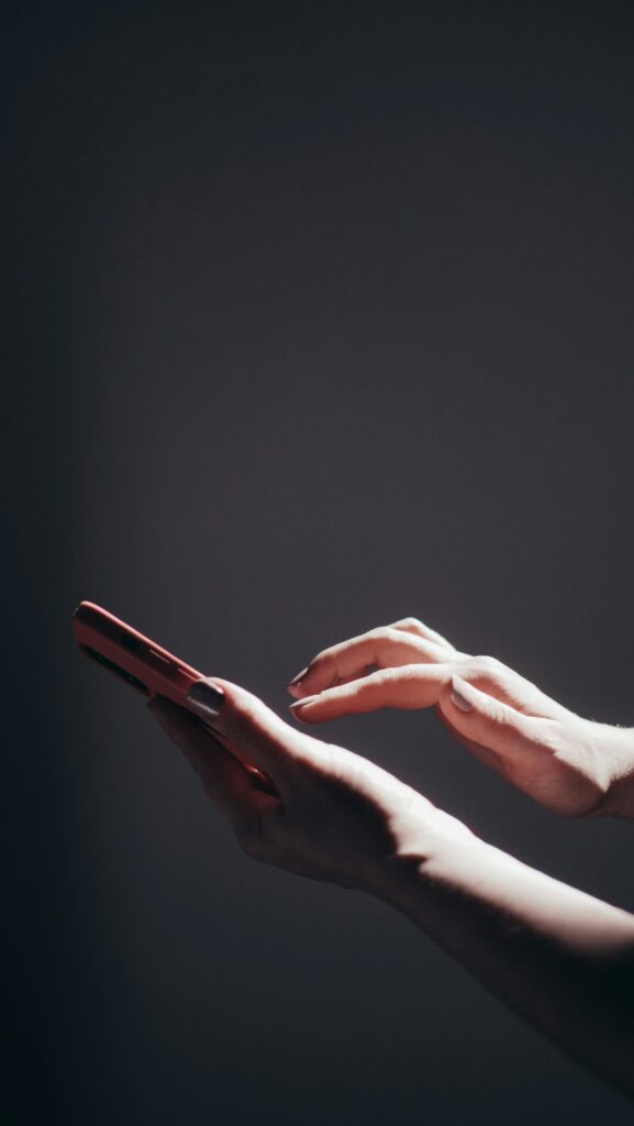 Close-up of hands holding a smartphone under dramatic lighting, highlighting modern technology use.